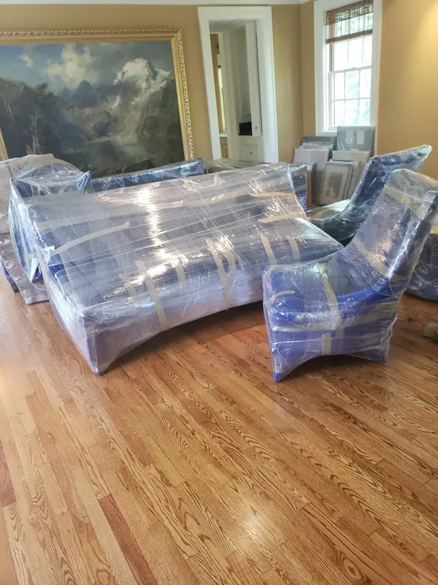 Living room furniture wrapped in moving blankets and plastic before an apartment move